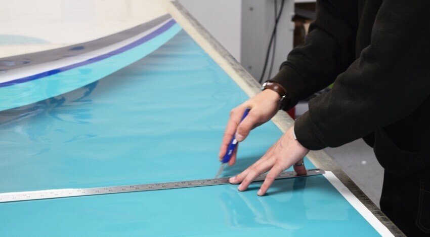 Vehicle wrap technician cutting vinyl before installation onto a Mercedes lorry.