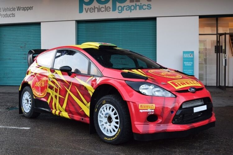 Red and yellow motorsport livery and vinyl graphics on Ford Fiesta R5 rally car outside Popin in Cardiff.