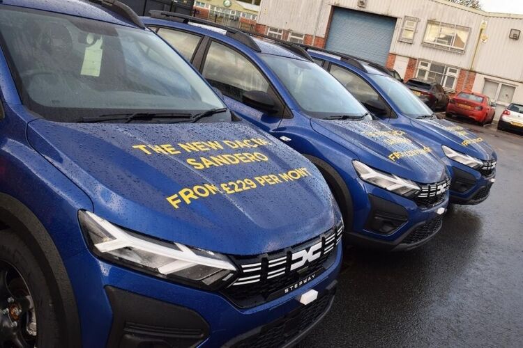 Yellow marketing vehicle vinyl graphics on the bonnets of three blue company owned Dacia Sandero cars.