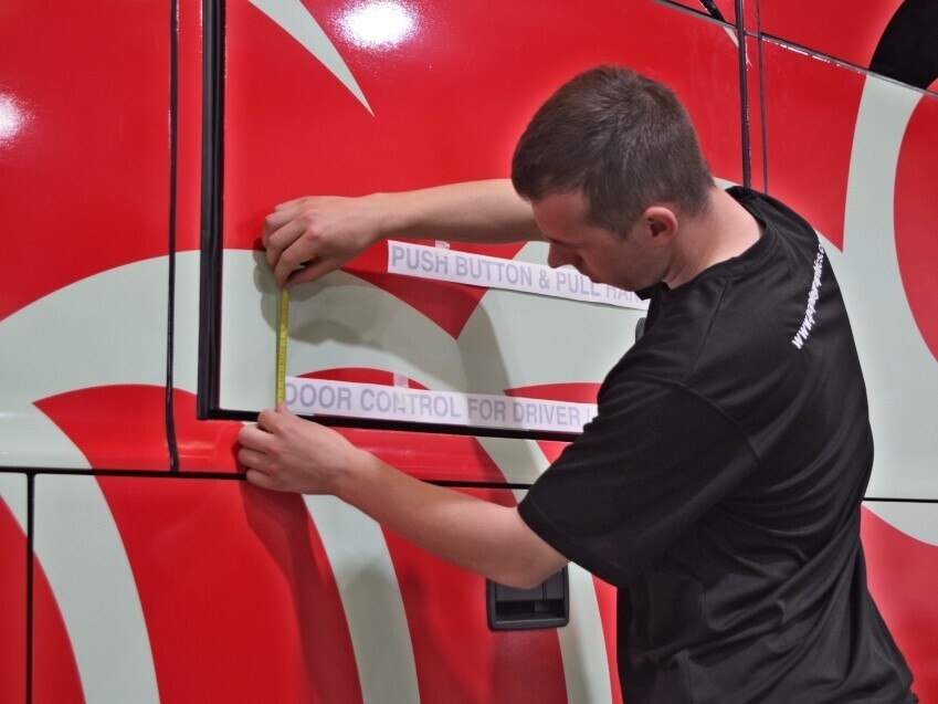 Vehicle graphics specialist installing vinyl graphic onto a coach.