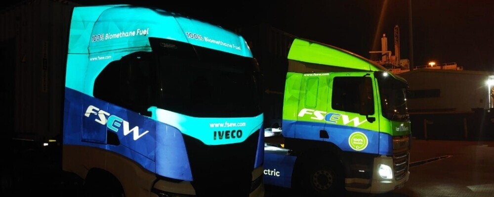 Reflective vinyl vehicle graphics on two trucks glowing at night under headlights.