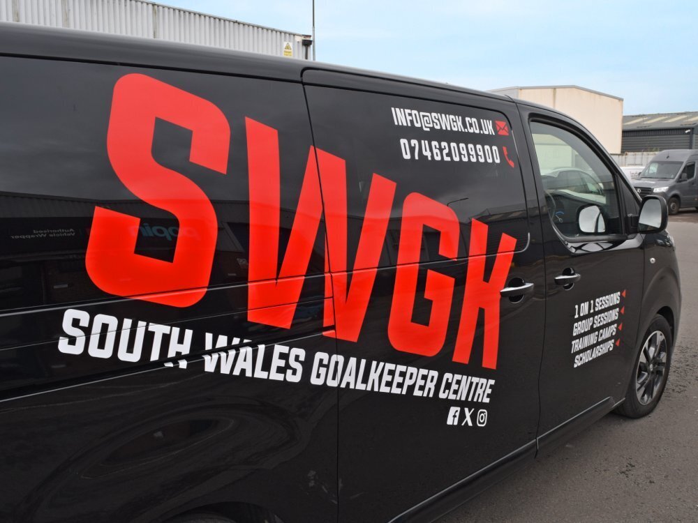 Large red and white company branded vinyl graphics on black Vauxhall Vivaro van.