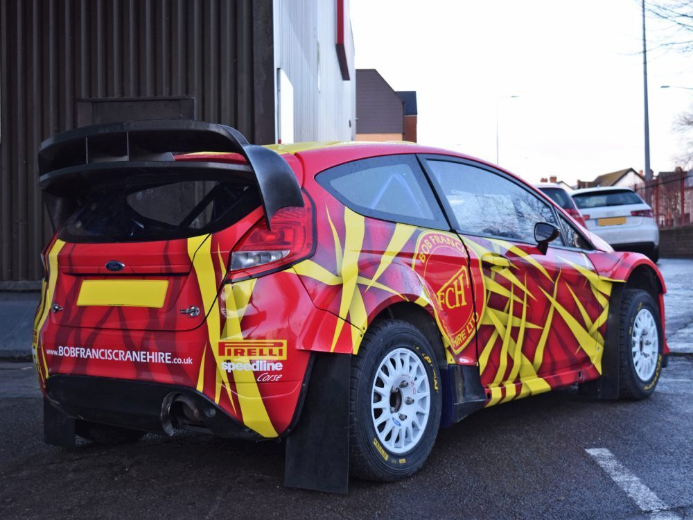 Bright red and yellow commercial wrap on Ford Fiesta R5 business car.