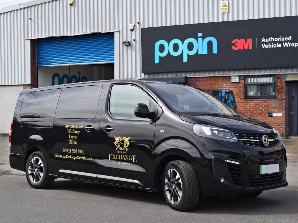 Gold vinyl graphics on black Vauxhall Vivaro company van outside Popin in Cardiff.