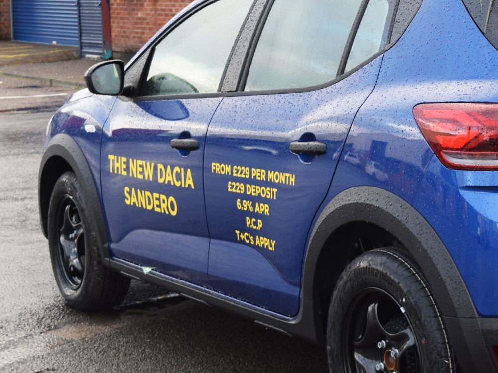 Yellow vinyl graphics on blue Dacia Sandero company car.