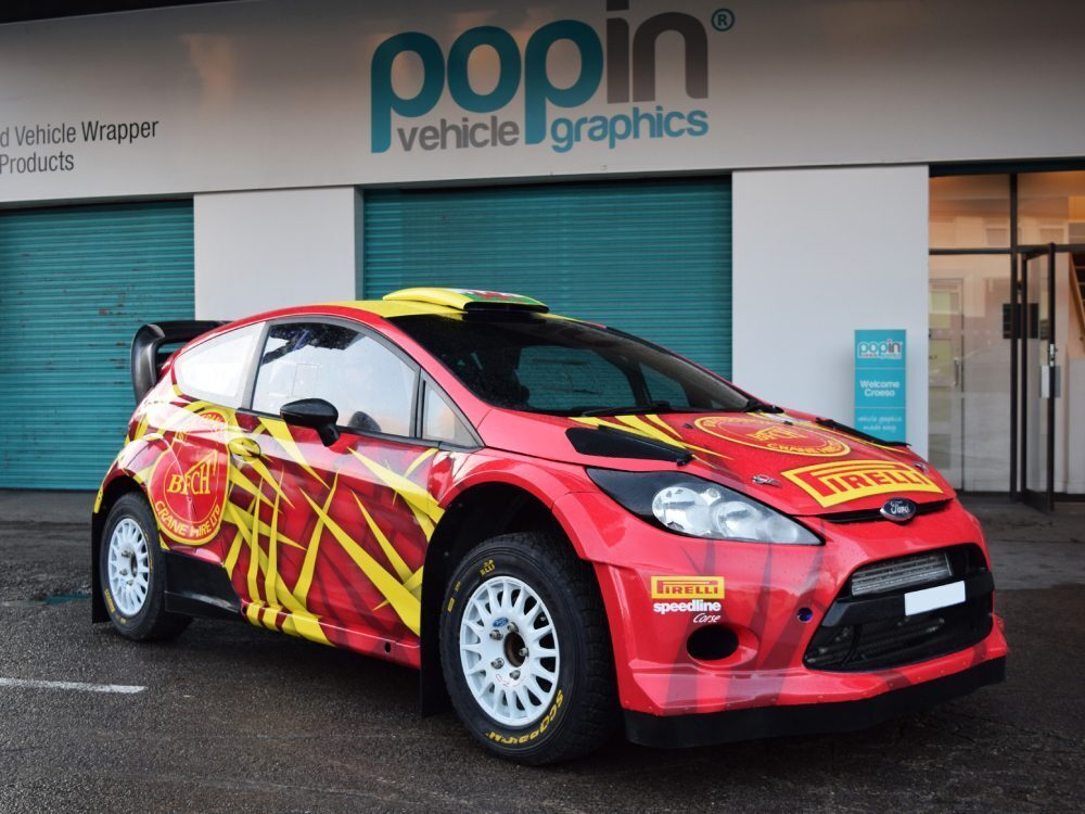 Red and yellow commercial wrap on Ford Fiesta R5 company car.