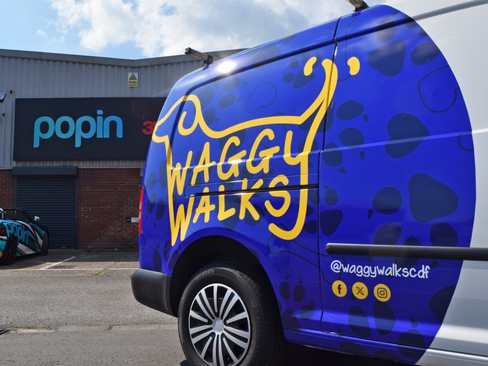 Volkswagen Caddy Maxi with rear partial branded blue and yellow Waggy Walks van wrap outside Popin in Cardiff.