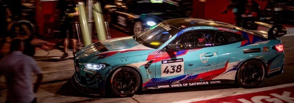 BMW motorsport car entering pit stop during a night race.