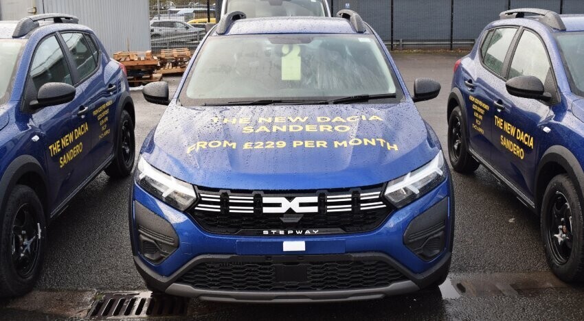 Blue company Dacia Sandero car with yellow marketing vinyl graphics.
