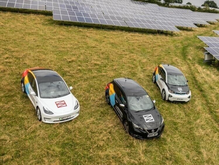 Fleet of company cars with branded vehicle liveries and graphics parked on grass near solar panels.