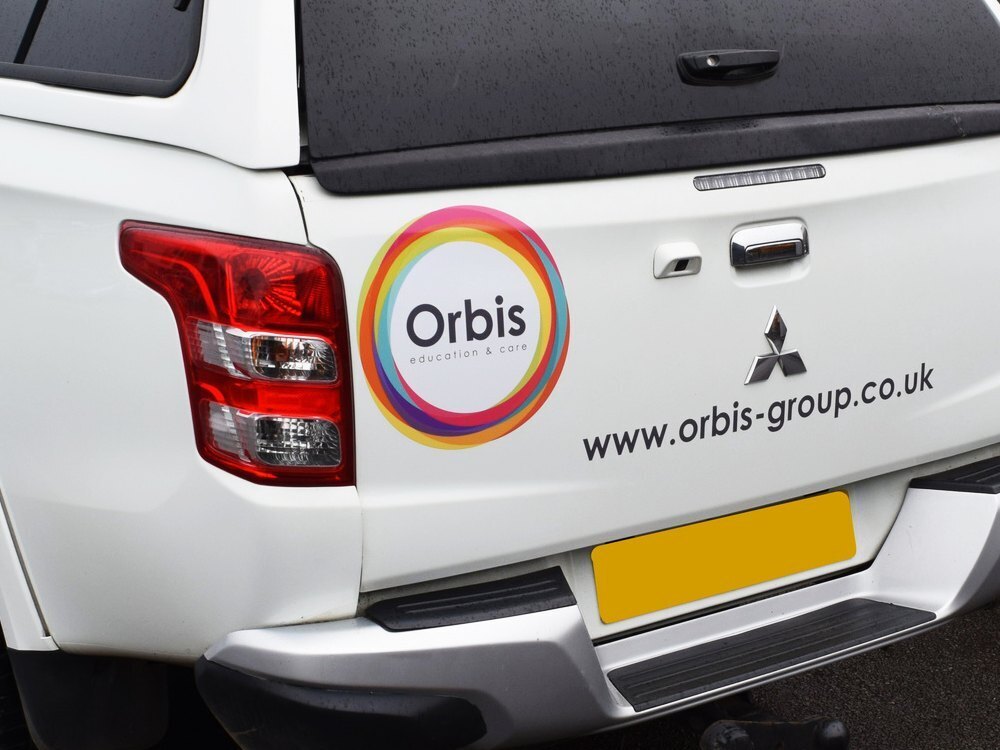 Branded vehicle graphics on rear of white company Mitsubishi L200.