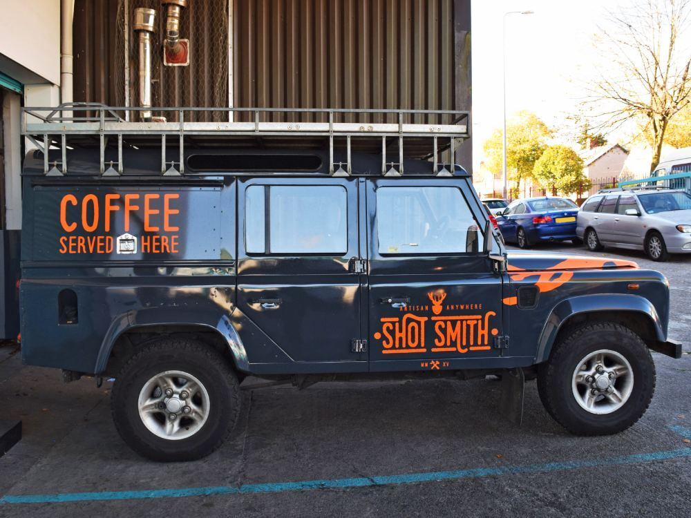 Company owned blue Land Rover Defender with orange vinyl graphics.