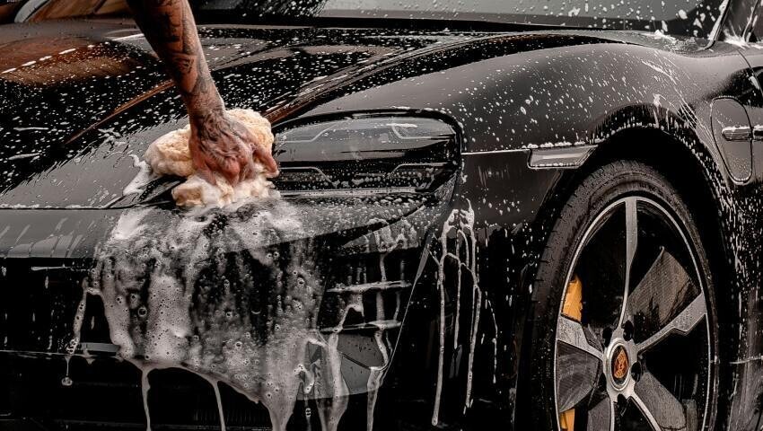 Cleaning a black Porsche race car during preparation for motorsport livery installation.