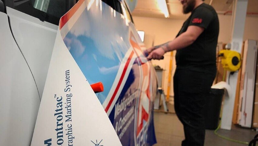 Expert vinyl wrap installer applying motorsport livery to a race car.