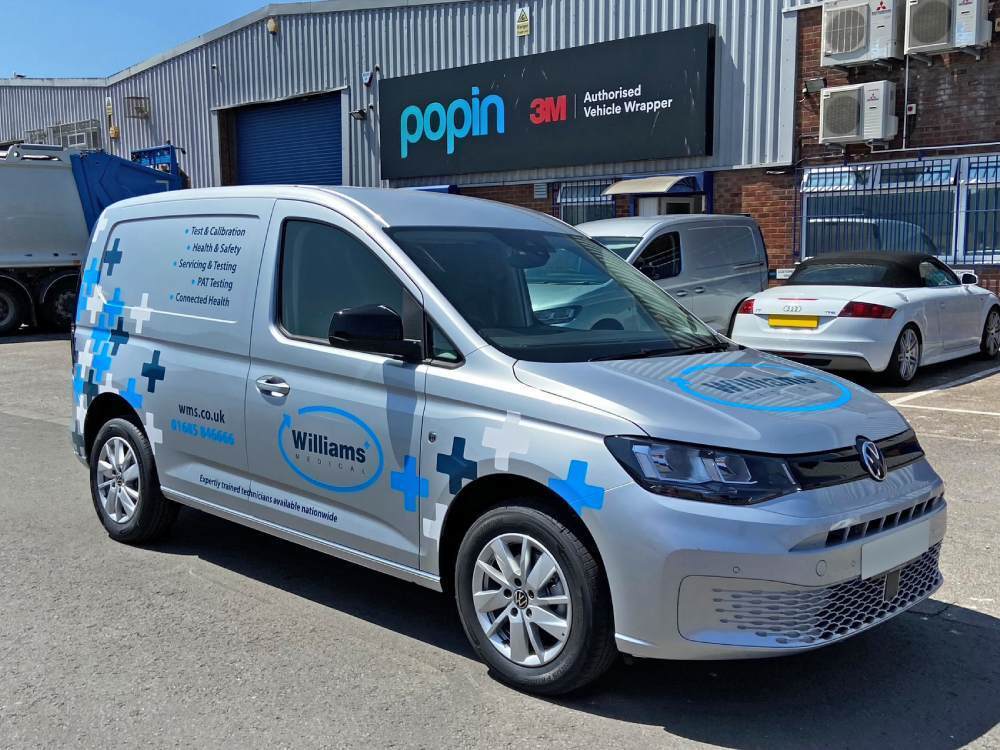 Silver Volkswagen Caddy with branded partial van wrap and graphics outside Popin in Cardiff.