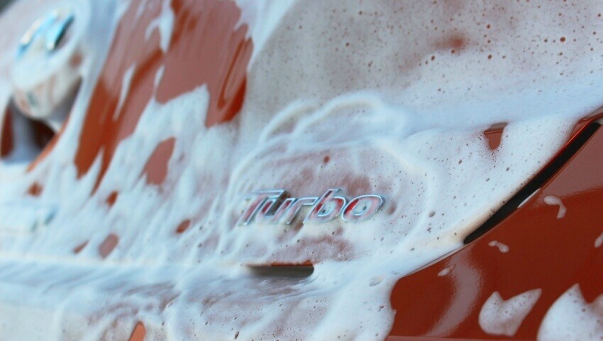 Red turbo motorsport car covered in soapsuds while being washed between races.