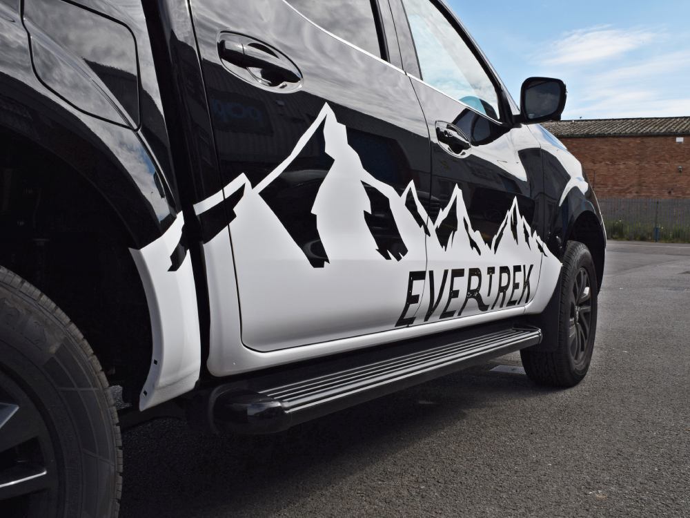 Close up of mountain themed branded vehicle graphics on door of black company Nissan Navara.