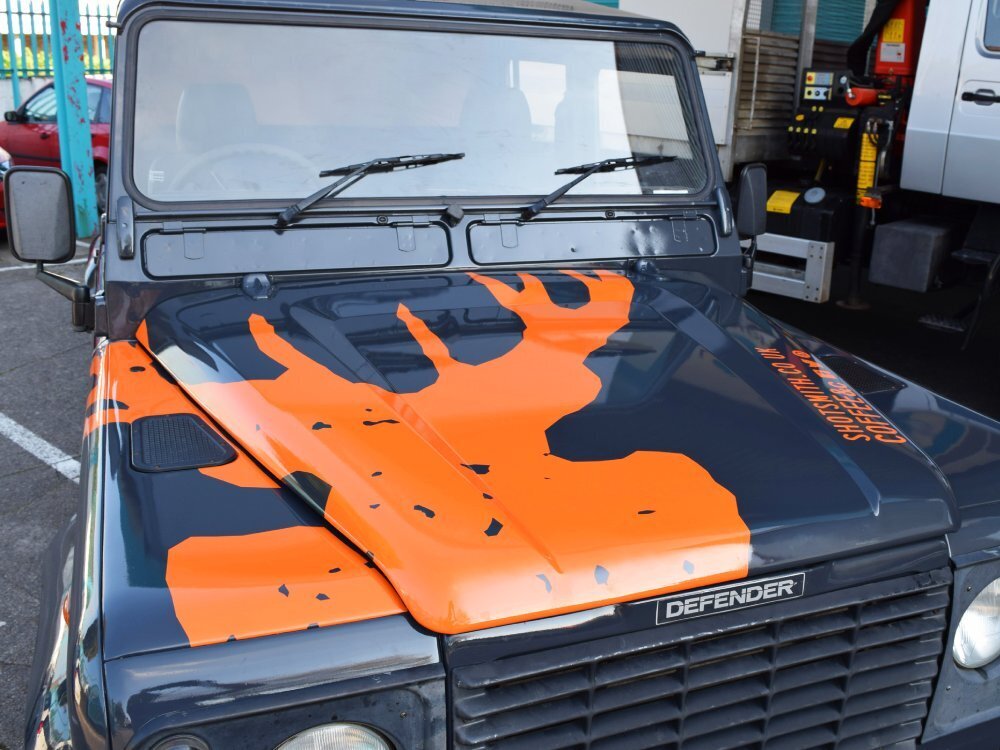 Orange branded vinyl graphics on blue company Land Rover Defender.