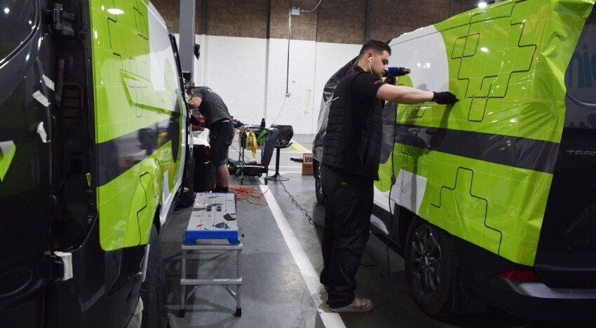Branded vehicle wraps being installed onto Ford company vans.