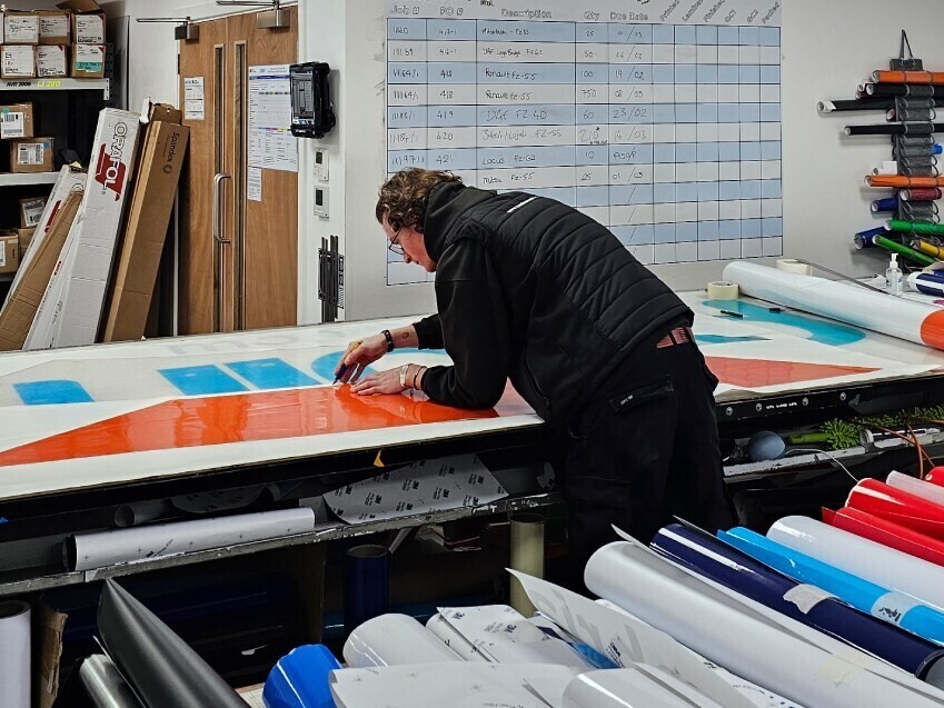 Technician precisely cutting a vehicle vinyl graphic before installation on a van.