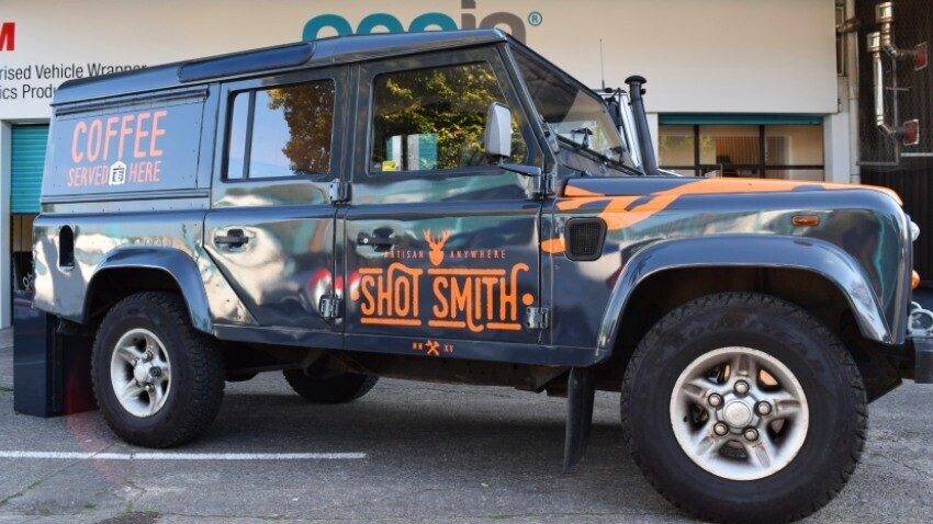 Company owned Land Rover Defender with orange business branded vinyl graphics outside Popin vehicle wrap centre in Cardiff.
