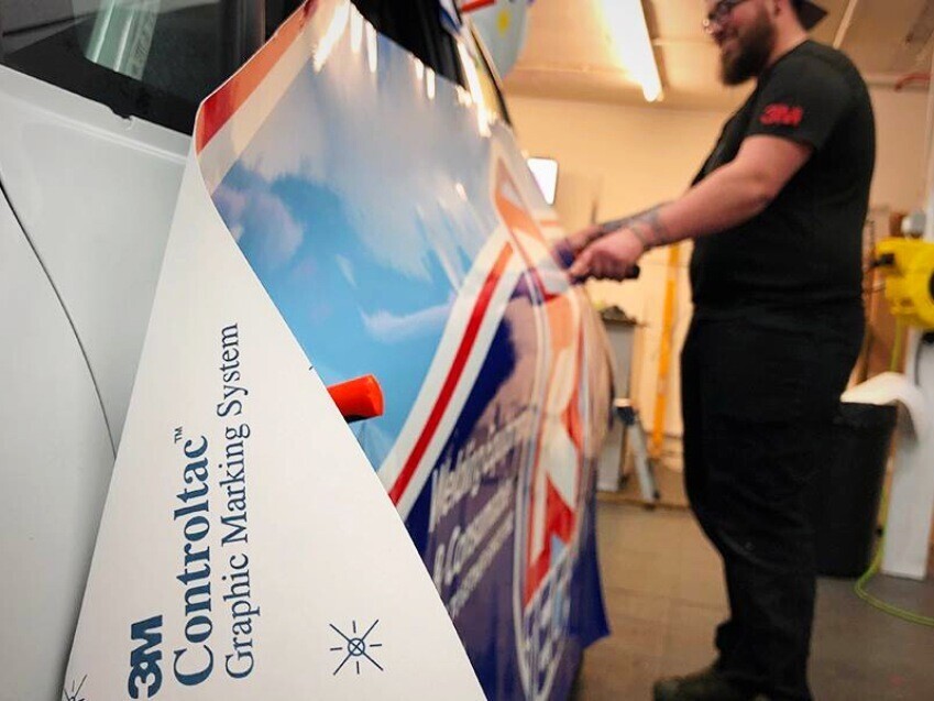 Popin Graphics technician expertly installing a 3M premium vinyl vehicle wrap onto a company car.