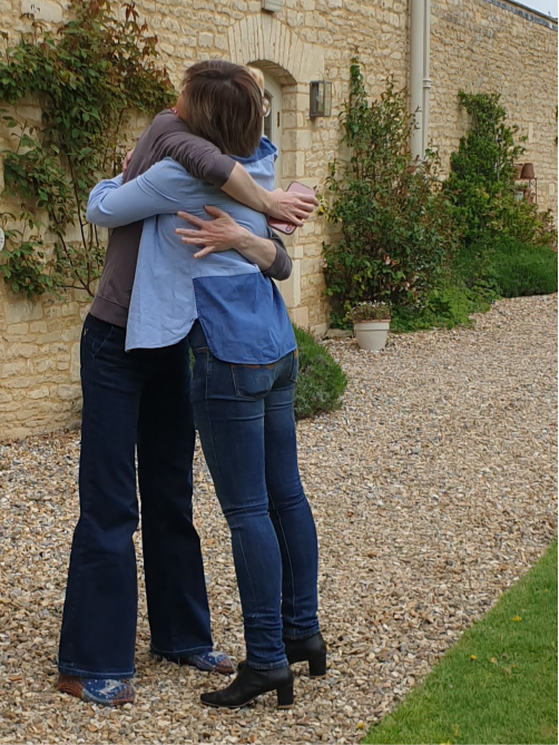 Two women hugging outside a country house.