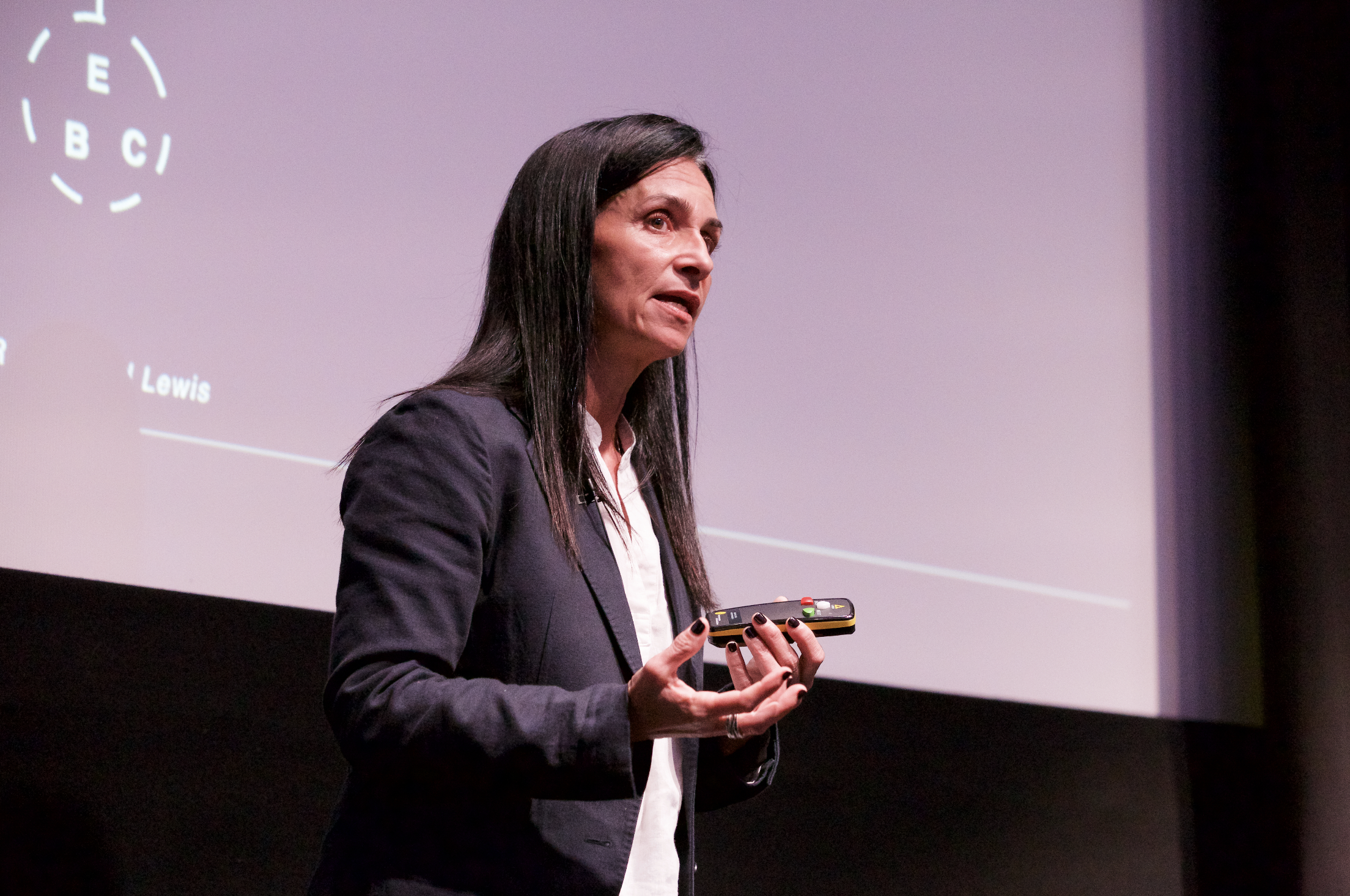 A speaker on stage holding a clicker and speaking passionately in front of the screen.
