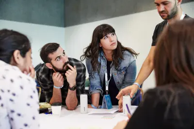 Three women and man sat a table, listening intently to a man standing.