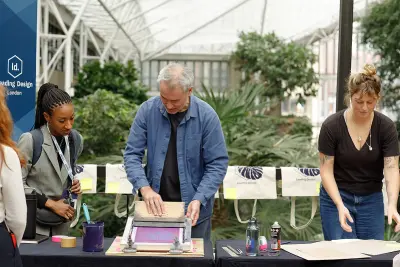 Three people running a hands-on printmaking activity at a Leading Design London event, set inside a bright indoor greenhouse space.