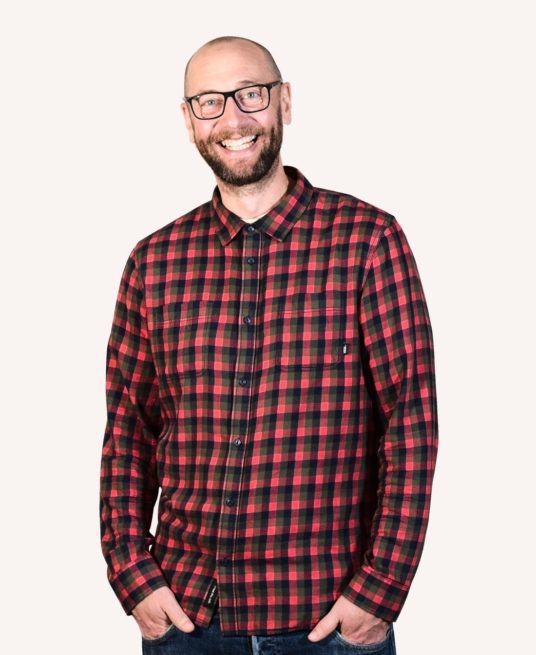 Andy smiles wearing a red checked shirt, he is very tall