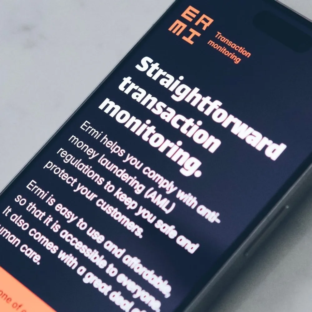 A shallow-focus photograph of an iPhone showing the new Ermi home page design. The phone is lying flat on a smooth, light marble surface.
