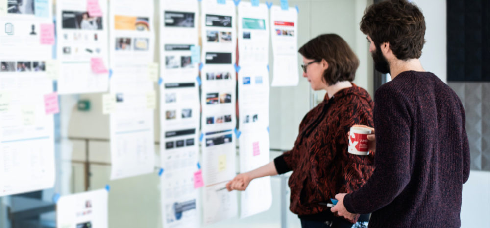 Jo and Hayden looking at a wall of web pages and post its