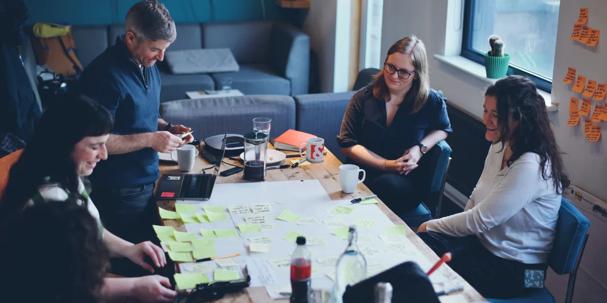 A photo of the Clearleft team and the Inventory Planner team sat around a table working on a project. They are prioritising product features using Post-its.