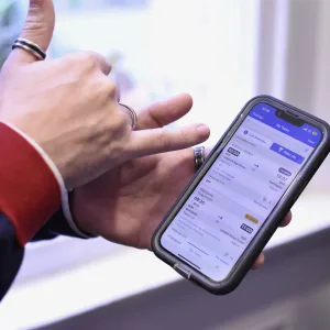 Two hands using a smartphone one hand holding the phone and another hand pointing at something on the screen with their little finger.