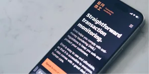 A shallow-focus photograph of an iPhone showing the new Ermi home page design. The phone is lying flat on a smooth, light marble surface.