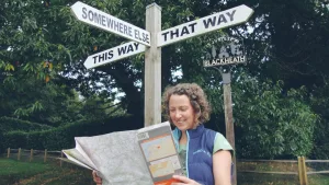 A woman is looking at a map in front of a wayfinding sign with points to three directions: this way, that way, somewhere else.