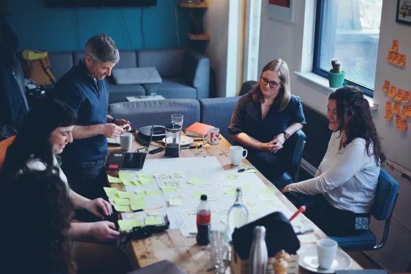 A photo of the Clearleft team and the Inventory Planner team sat around a table working on a project. They are prioritising product features using Post-its.