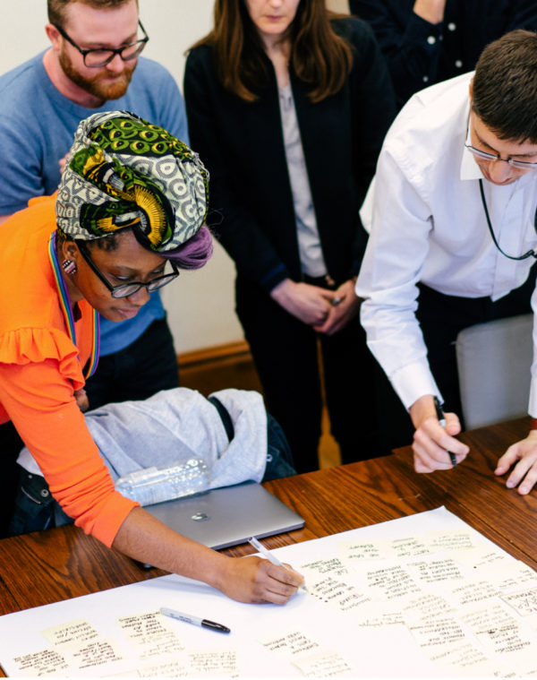 A group of designers gathered round a table collaborating on a large sheet of paper with sharpies.
