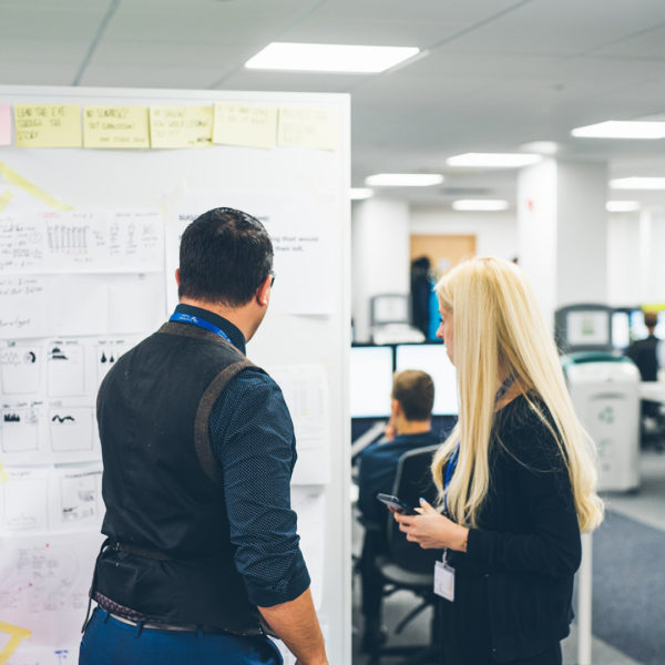 Man and woman in office looking at wall of design sketches and journey maps
