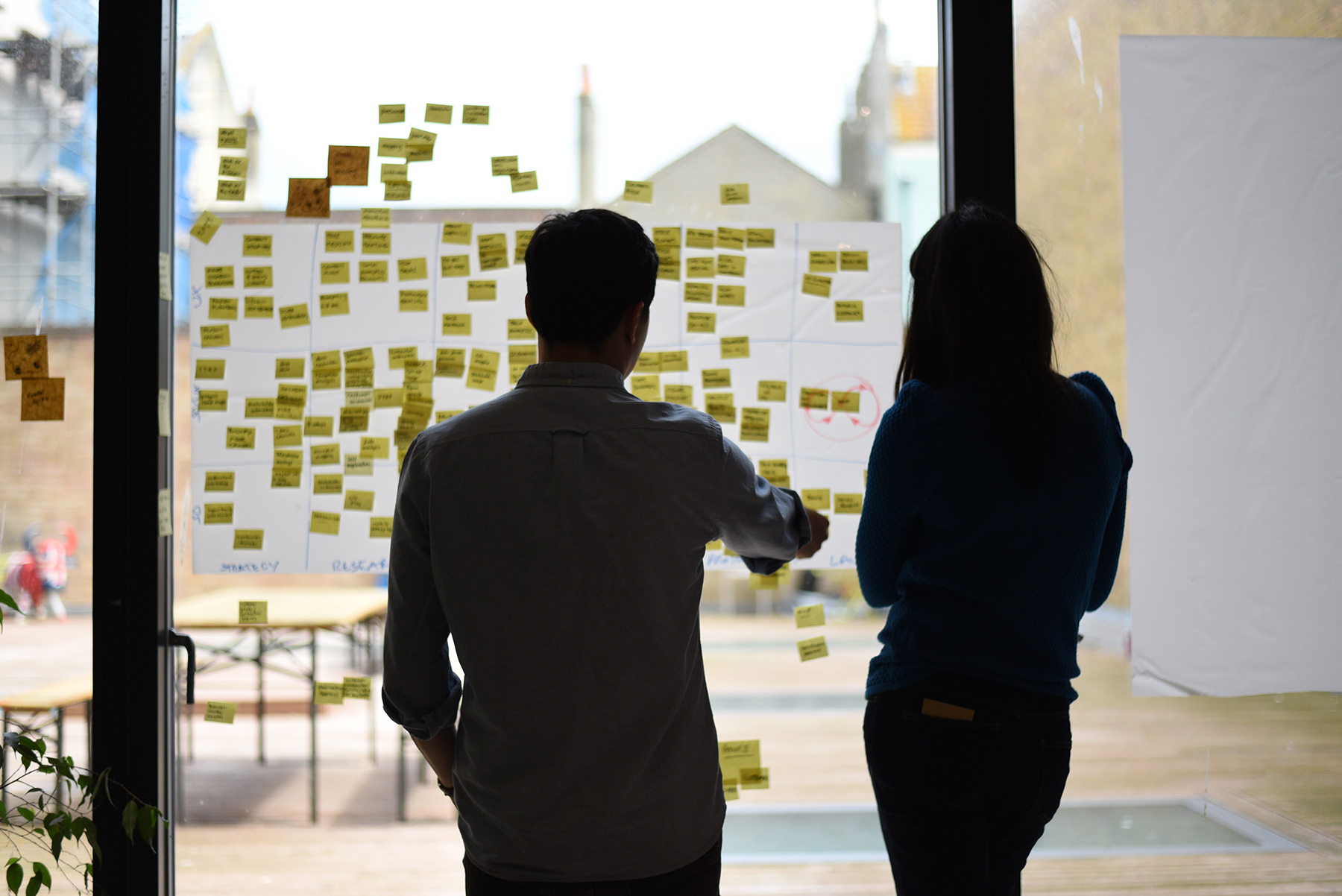 Two people having a discussion in front of a wall of post-it notes.