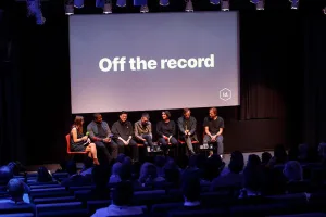 Day 2 speakers seated on stage in front of a large screen reading ‘Off the record,’ addressing an audience in a dimly lit auditorium.