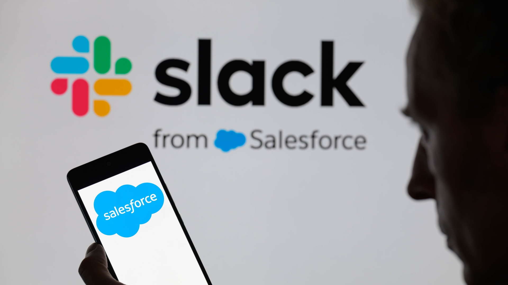 Логотип Salesforce отображается на смартфоне, а на заднем плане — логотип Slack