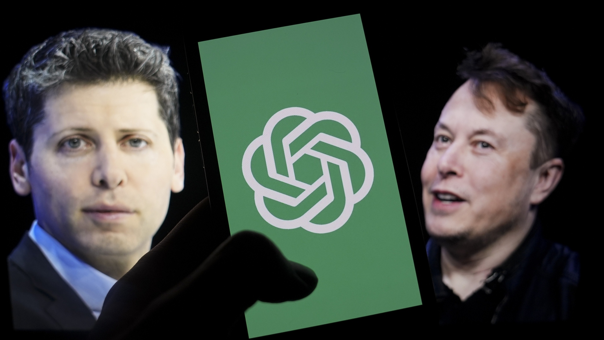 Логотип 'OpenAI' отображается на экране мобильного телефона перед экраном компьютера, на котором отображаются фотографии Илона Маска и Сэма Альтмана.