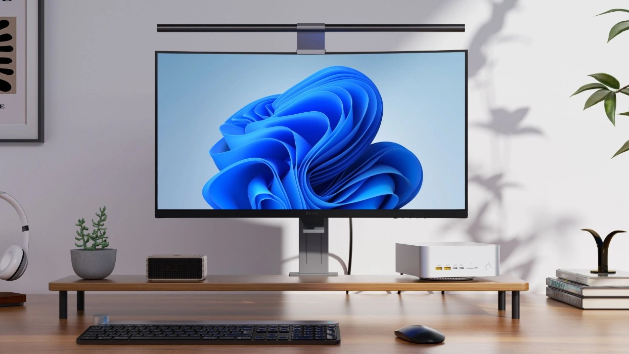 Geekom A9 Mega mini PC on a desk showing the Windows 11 wallpaper on the monitor.