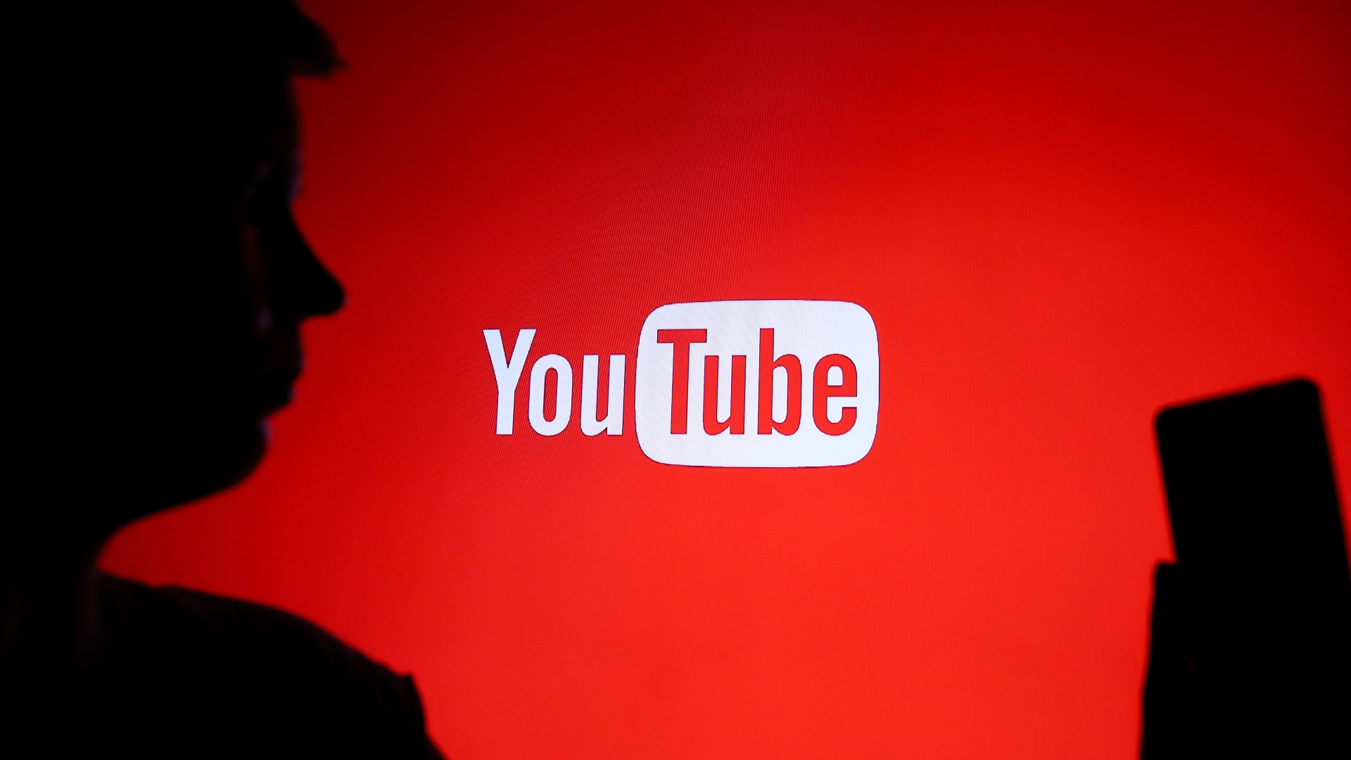 Человек держит телефон на фоне логотипа YouTube.