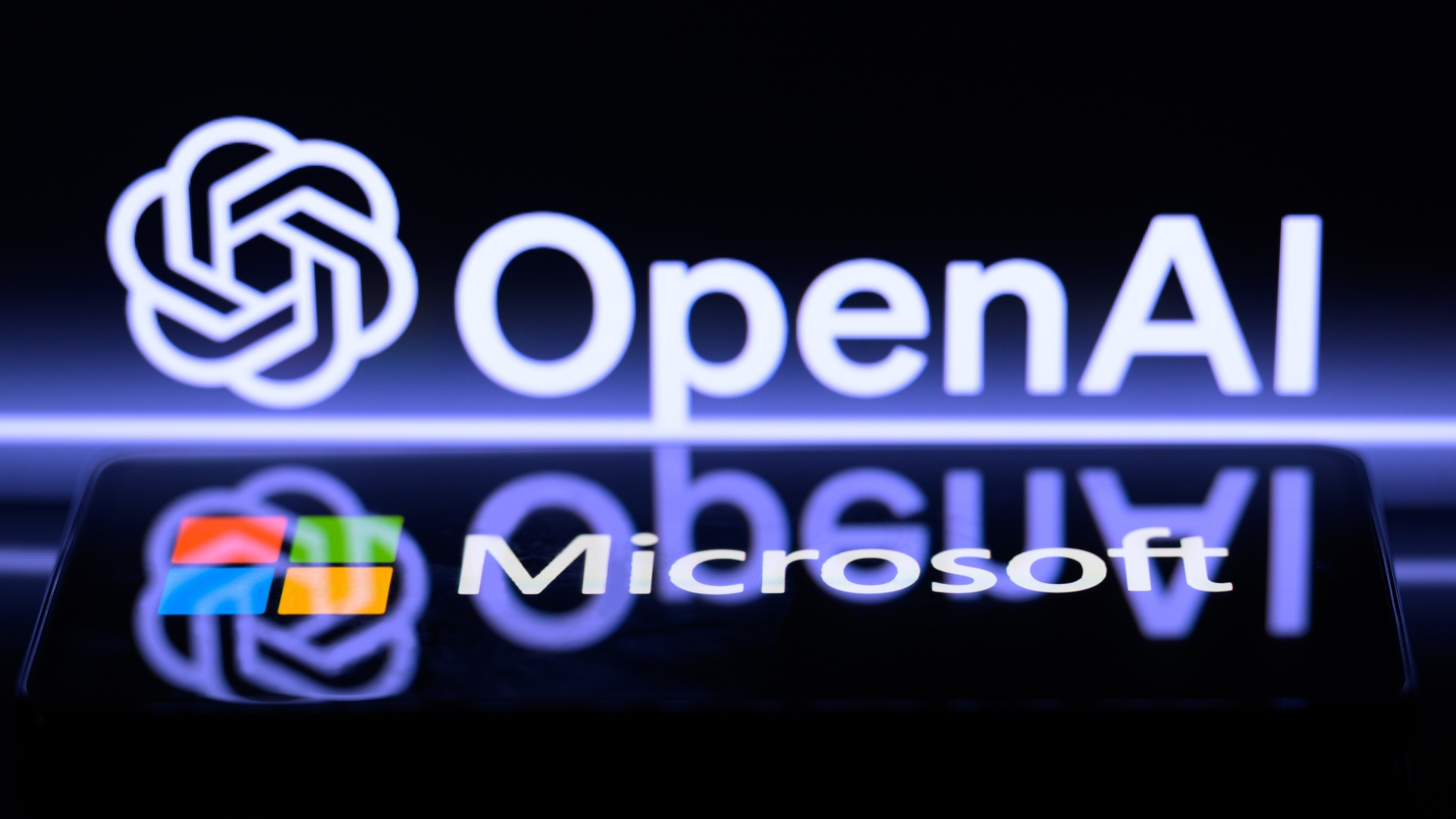 Логотип Microsoft отображается на смартфоне, а логотип OpenAI виден на экране на заднем плане.