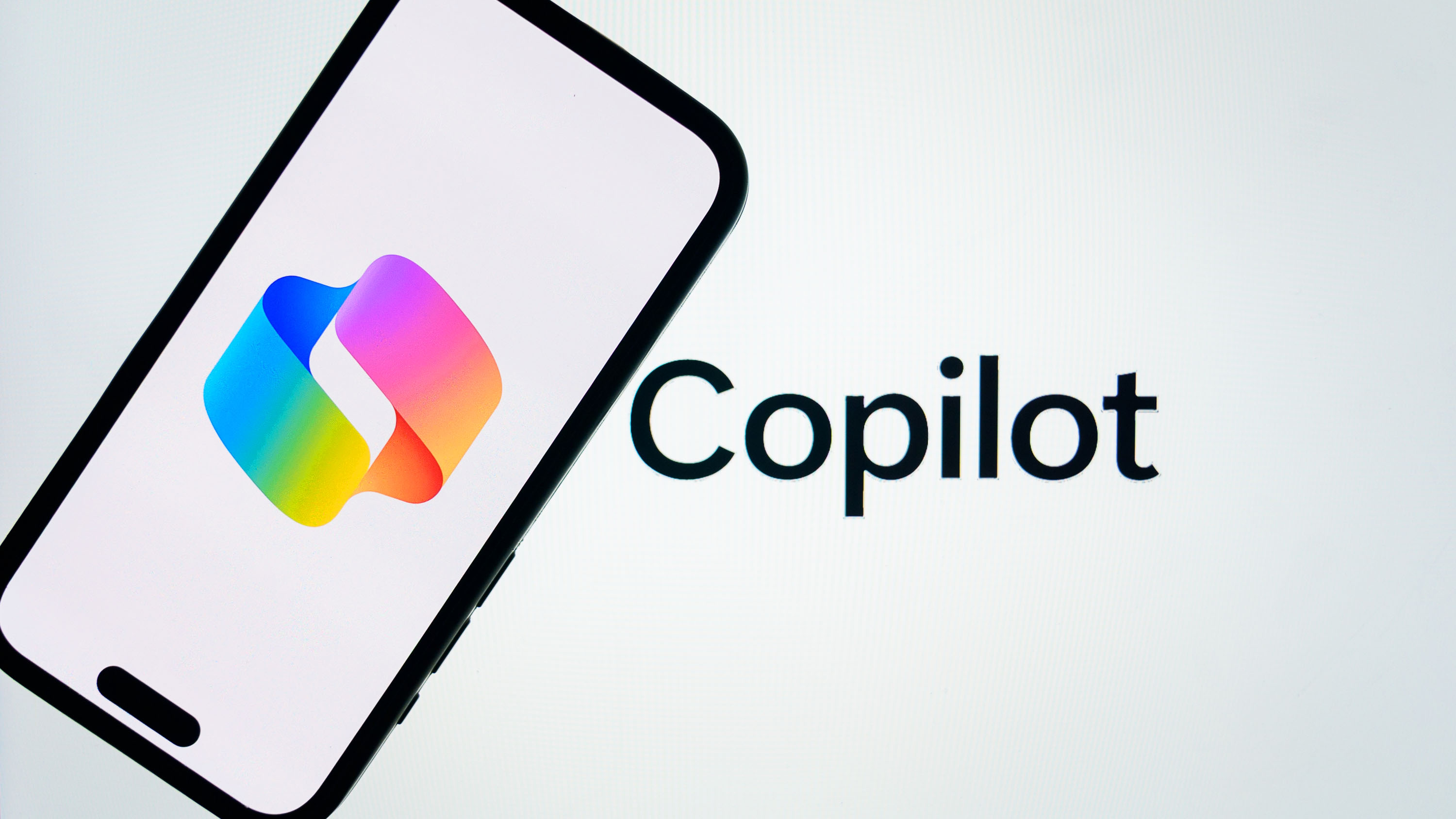 Логотип Microsoft Copilot отображается на экране мобильного телефона перед экраном с надписью Copilot в Анкаре, Турция, 14 марта 2025 года.
