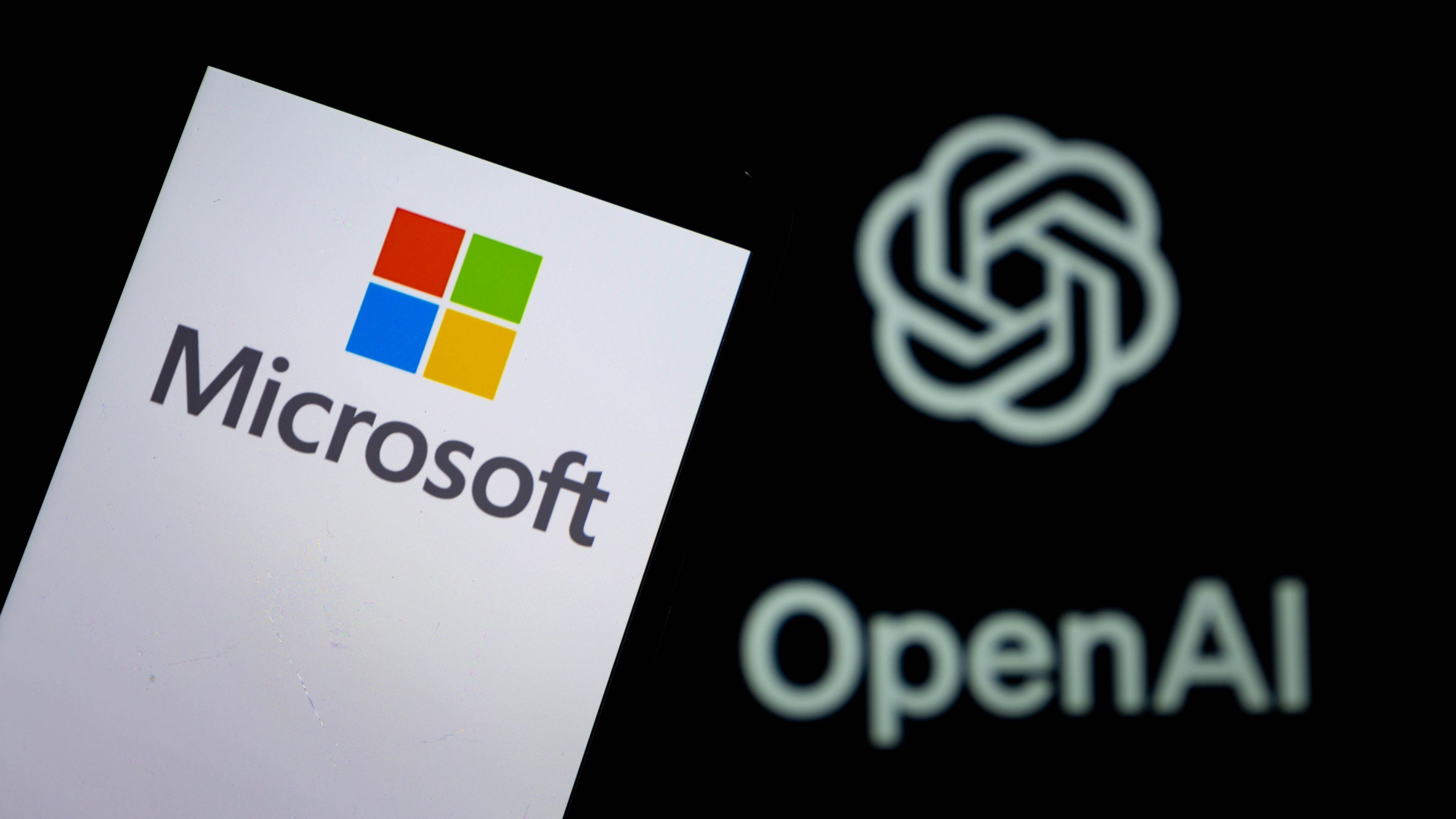 Логотип Microsoft, отображаемый на смартфоне с логотипом OpenAI на заднем плане.