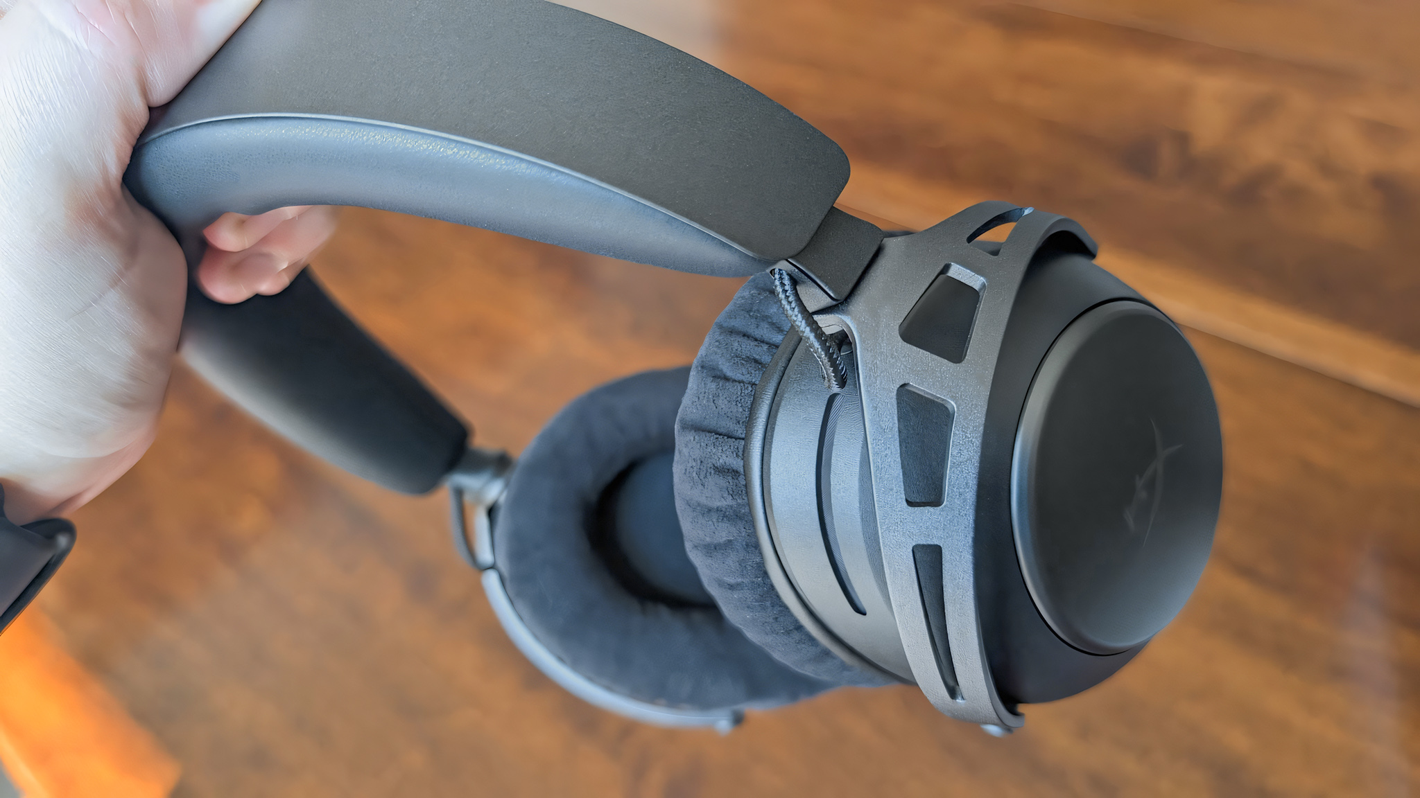 Рука держит беспроводную игровую гарнитуру HyperX Cloud Alpha 2 Wireless за оголовье.